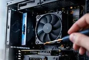 Hand with a screwdriver working inside an open desktop PC next to a cooling fan